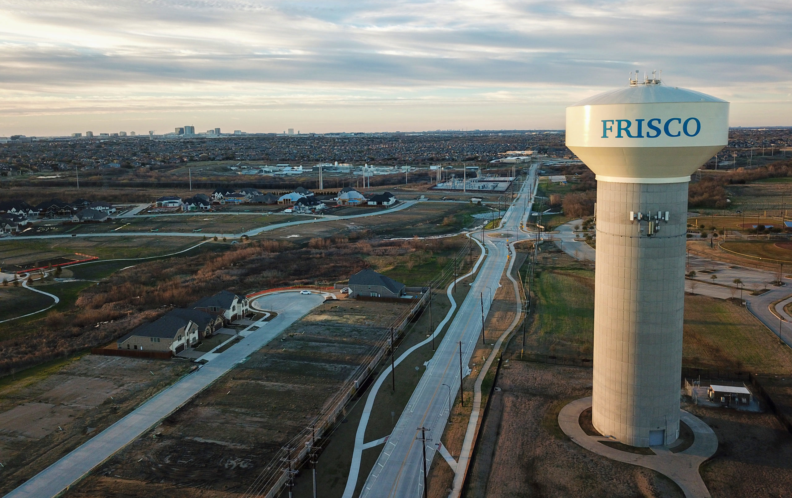 An aerial view of new subdivisions being developed in Frisco, Texas. A Frisco water tower is in the foreground and office towers are on the horizon.
